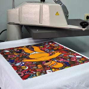 Peut inclure: Un t-shirt blanc avec un motif graphique color&eacute; repr&eacute;sentant un personnage de dessin anim&eacute; jaune entour&eacute; d'aliments. Le t-shirt est sur une presse &agrave; chaud, sugg&eacute;rant un processus d'impression personnalis&eacute;.