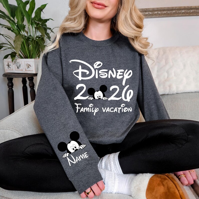 May include: A dark gray sweatshirt with the text "Disney 2020 Family Vacation" in white. A Mickey Mouse graphic is between the numbers. The sleeve features a Mickey Mouse graphic and the word "Name".
