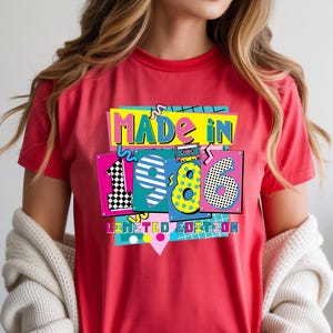 May include: A red t-shirt with a colorful graphic that says "MADE IN 1986 LIMITED EDITION." The graphic has a retro 80s design with bright colors and geometric shapes. The shirt is short-sleeved.