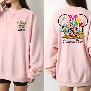 May include: Light pink sweatshirt featuring a Disney character design on the front and back. The front displays a group of characters with the word "Name" below. The back features a larger design with "Custom Text".