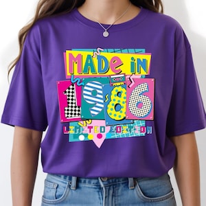May include: A purple t-shirt with a colorful graphic design that says "MADE IN 1986 LIMITED EDITION." The design features the numbers 1, 9, and 6 in different patterns and colors, with a cassette tape illustration.