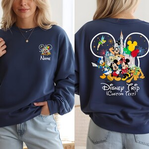 May include: Navy blue sweatshirt featuring Disney characters. The front displays a small Mickey Mouse head design with characters and the name "Name". The back showcases a larger Mickey Mouse head with Disney characters, a castle, and the text "Disney Trip (Custom Text)".
