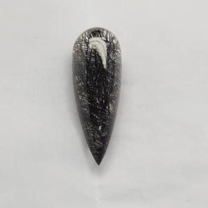 以下が含まれることがあります： 黒いクモの巣のような模様が内包された、透明な涙型のペンダント。 ペンダントは尖った先端と丸みを帯びた上部を持ち、上部近くには小さな白いインクルージョンがあります。 全体的に、光と影のコントラストが印象的です。