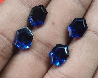 May include: Four loose, faceted, hexagon-shaped blue gemstones with a deep, saturated color and reflective surfaces. Each stone features a precise geometric cut with multiple facets that catch the light, displaying varying shades of royal blue.