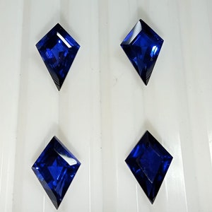 May include: Four dark blue, faceted, kite-shaped gemstones on a white background.