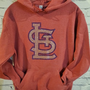 May include: Red hooded sweatshirt with a large rhinestone-embellished "LS" logo in gold and purple.