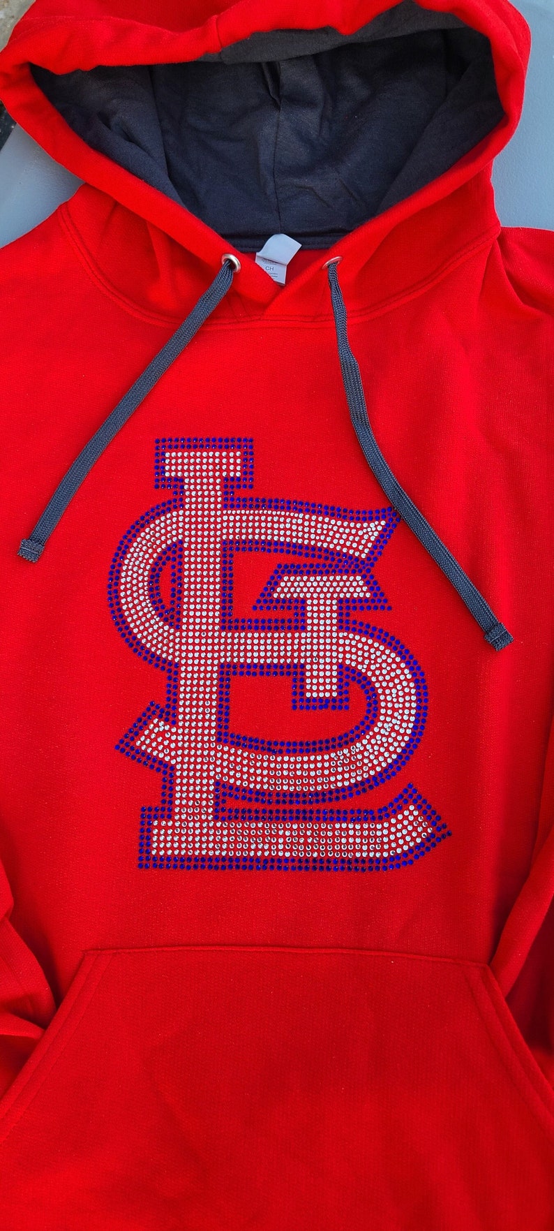 May include: Red hooded sweatshirt with a large, white and blue rhinestone 'LS' logo on the front.