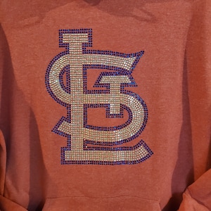 May include: A rust-colored hoodie with a large, sparkly, navy blue and gold "STL" logo on the front.