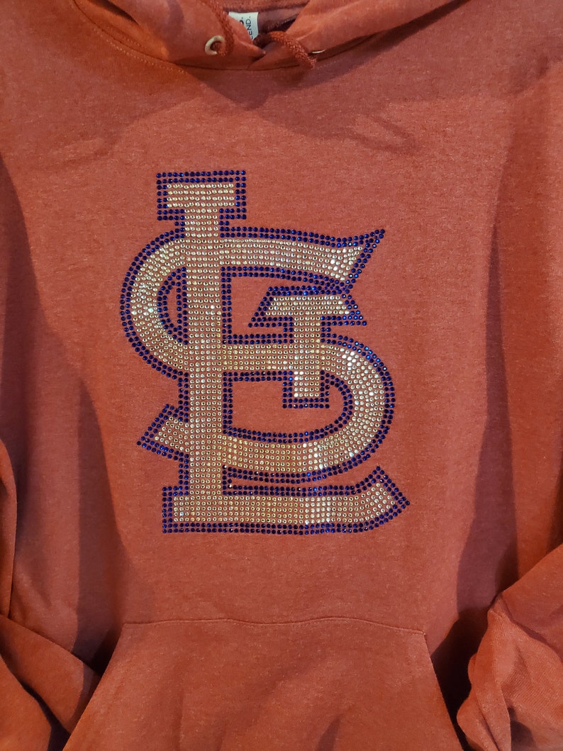 May include: A rust-colored hoodie with a large, sparkly, navy blue and gold "STL" logo on the front.