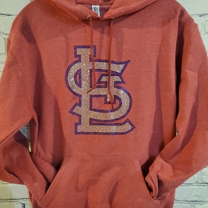 May include: Red hooded sweatshirt with a large rhinestone design of the St. Louis Cardinals logo in gold and purple.