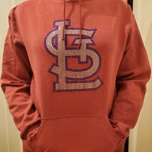 May include: A red hoodie with a large, sparkly, blue and gold "LS" logo on the front. The hoodie has a drawstring hood and a kangaroo pocket.