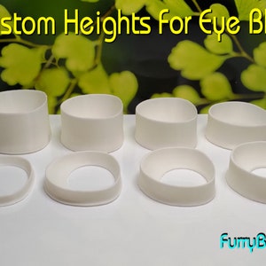 Puede incluir: Ocho blancos de ojos de plástico blanco de diferentes alturas. Los blancos de ojos están dispuestos en dos filas sobre una superficie blanca. El texto "Custom Heights for Eye Blanks" es visible en la parte superior de la imagen.