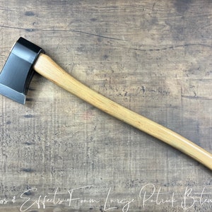 Peut inclure: Une hache noire et brune avec un manche en bois. La hache est sur une surface en bois.