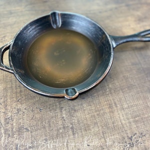 May include: A black cast iron skillet with a brown interior and a single handle. The skillet is sitting on a wooden surface.