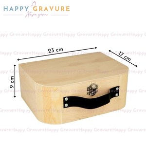 Puede incluir: Una caja de almacenamiento de madera clara con un asa negra y un cierre de metal. La caja tiene unas dimensiones de 23 cm de largo, 17 cm de ancho y 9 cm de alto. La superficie muestra vetas de madera natural y el texto Happy Gravure.