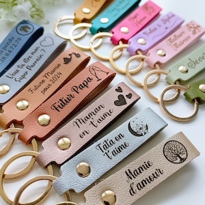 May include: A collection of multi-colored faux leather keychains featuring gold-tone metal rings and rivets. Each strap is engraved with various French phrases, names, and icons such as hearts, a tree, a moon, and champagne glasses.