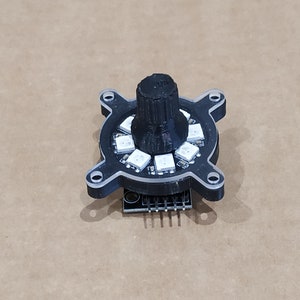 May include: A black and white circular LED light with a black knob on top. The light is mounted on a black circuit board with a row of pins.