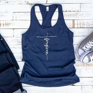 Könnte beinhalten: Ein marineblaues Tanktop mit einem weißen Kreuz und dem Wort "forgiven" vertikal auf dem Kreuz geschrieben.