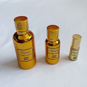 May include: Three gold bottles with black labels that read "Fatima Collection". The bottles are different sizes and are arranged from largest to smallest.
