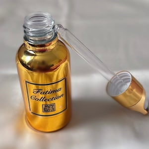 May include: A gold bottle with a dropper top. The bottle has a black label that says "Fatima Collection" and a black square with a design inside.