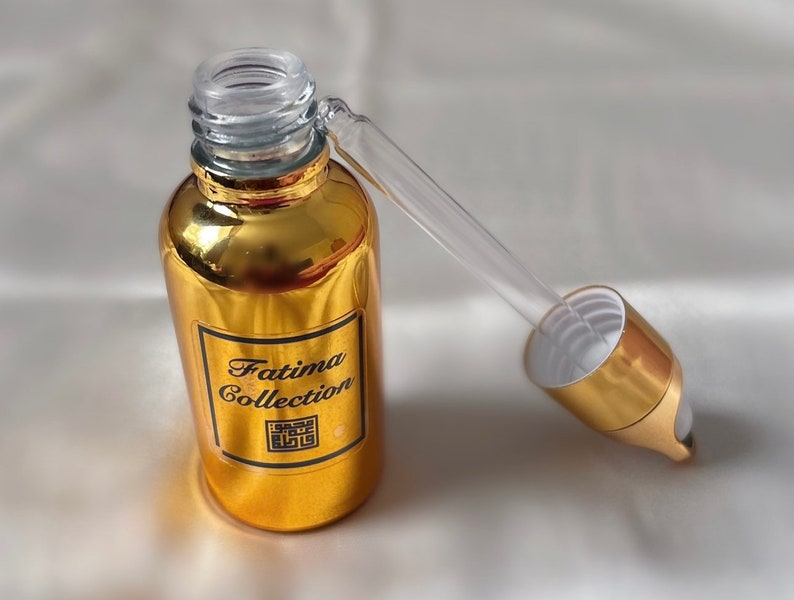 May include: A gold bottle with a dropper top. The bottle has a black label that says "Fatima Collection" and a black square with a design inside.