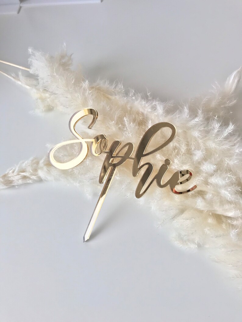 Pu&ograve; includere: Topper per torta in acrilico a specchio dorato con il nome "Sophie" scritto in corsivo.