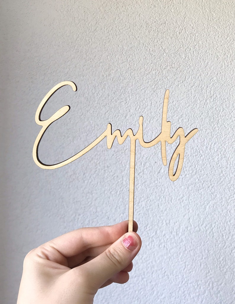 Pu&ograve; includere: Un topper per torta in legno con il nome "Emily" scritto in corsivo.