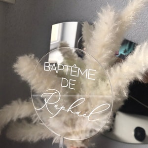 May include: Clear acrylic circle sign with the text "BAPT&Ecirc;ME DE Rapha&euml;l" in white lettering.