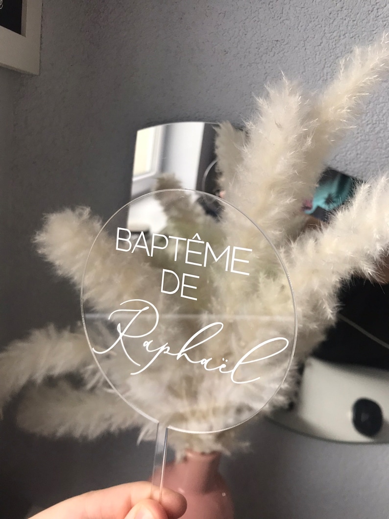 May include: Clear acrylic circle sign with the text "BAPT&Ecirc;ME DE Rapha&euml;l" in white lettering.