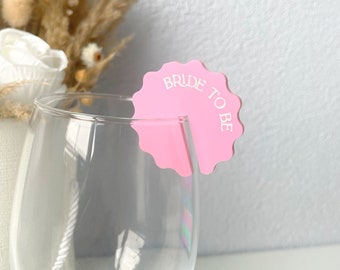 May include: Pink plastic glass charm with the text "Bride to Be" in white lettering.