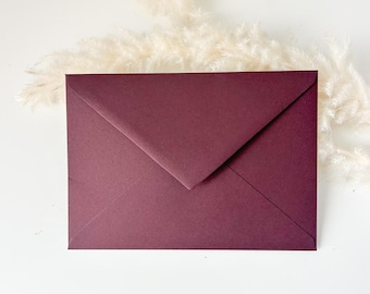 Può includere: Una busta color bordeaux intenso con una classica chiusura a patta triangolare. La busta è posizionata orizzontalmente, mostrando una texture di carta liscia e opaca con bordi netti e definiti, presentando un colore solido e uniforme.