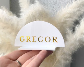 May include: White acrylic table number holder with a half-circle shape and a gold foil inscription that reads "GREGOR".