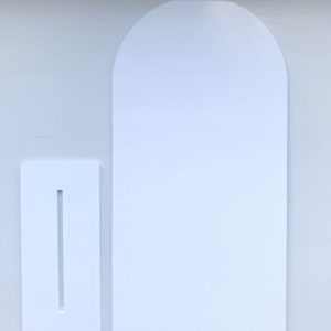 May include: White cardboard stand with a slot for a card or sign. The stand is shaped like a rectangle with a rounded top.