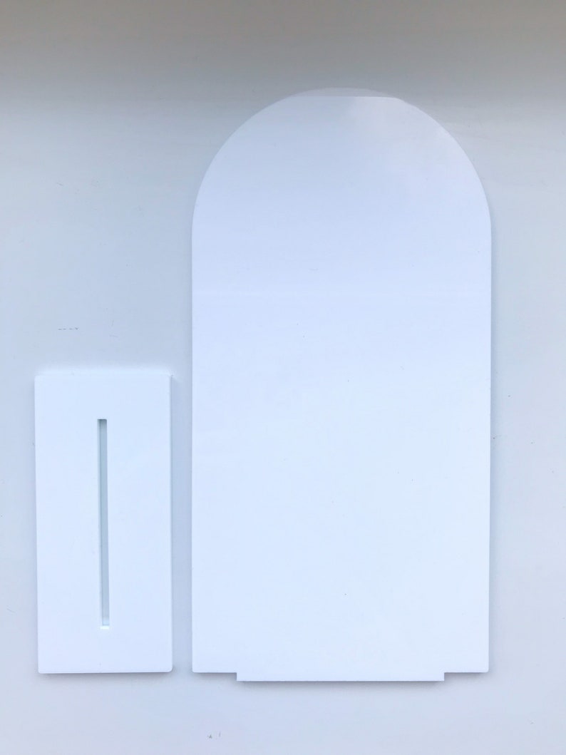 May include: White cardboard stand with a slot for a card or sign. The stand is shaped like a rectangle with a rounded top.