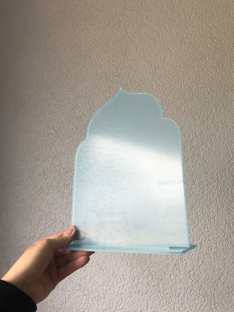 May include: A light blue glass bookend with a unique, abstract shape. The bookend has a small shelf at the bottom.