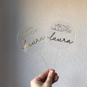 May include: Clear acrylic cake topper with gold lettering. The topper says "Happy Birthday Laura" and "V&scaron;etko Najlep&scaron;ie Laura".
