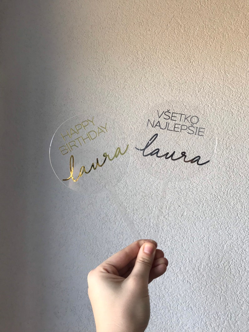 May include: Clear acrylic cake topper with gold lettering. The topper says "Happy Birthday Laura" and "V&scaron;etko Najlep&scaron;ie Laura".