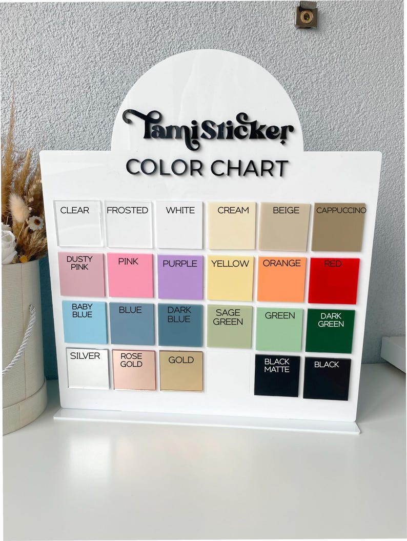 Op de afbeelding: Een witte acryl kleurenkaart display met de tekst "TamiSticker COLOR CHART". De kaart toont een raster van kleurstalen in verschillende tinten, waaronder helder, mat, wit, cr&egrave;me, beige en cappuccino.