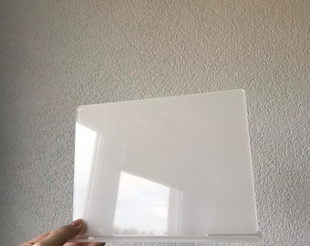 May include: A clear acrylic display stand with a rectangular shape. The stand is designed to hold a small object or photo.