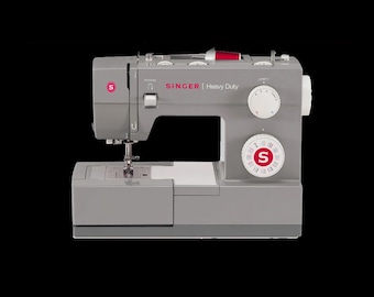 May include: A grey Singer Heavy Duty sewing machine featuring a red S logo, a needle, a presser foot, and two circular control dials on the front. The machine includes a white spool of thread on top and clearly displays the text SINGER Heavy Duty.