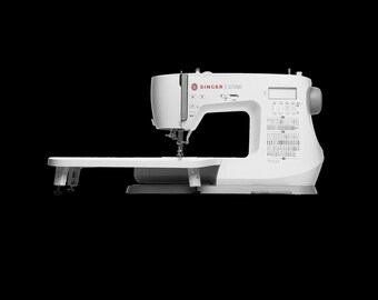 May include: A white Singer C7250 sewing machine featuring an extended flatbed work surface, a digital display screen, and a printed stitch pattern guide on the front panel. The machine includes a needle, presser foot, and handwheel.