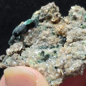 May include: A raw mineral specimen featuring a cluster of small, translucent, light-colored crystals interspersed with dark green, opaque mineral deposits. The rock formation has a rough, uneven texture with visible crystalline structures throughout.