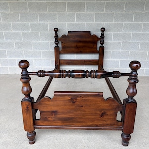 May include: A dark brown wooden bed frame featuring a headboard and footboard with curved top edges. The frame includes four tall, turned posts topped with spherical finials and a horizontal spindle rail connecting the front two posts.