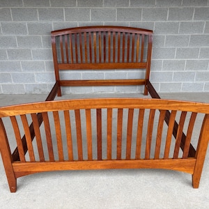 May include: A wooden bed frame with a headboard and footboard. The frame is made of a warm-toned wood and features vertical slats in both the headboard and footboard. The design is simple and classic, suitable for a bedroom.
