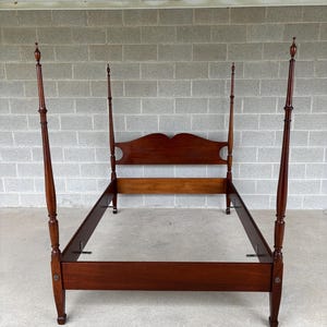 May include: A dark brown four-poster bed frame. The bed frame has four tall, slender posts with decorative finials. The headboard features a curved design. The frame is made of wood and has a classic, traditional style.