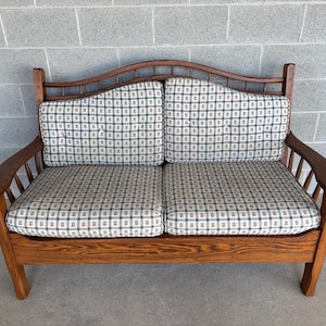 May include: A wooden loveseat with a dark brown finish. The seat cushions and backrests feature a patterned fabric in shades of blue, green, and cream. The arms are curved and the back has a decorative arch.