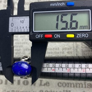 Op de afbeelding: Een zilveren ring met een grote, ovale, donkerblauwe lapis lazuli-steen. De ring wordt gemeten met een schuifmaat, die 15,6 mm aangeeft.