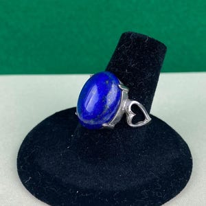 Op de afbeelding: Een zilveren ring met een grote ovale lapis lazuli-steen gezet in een hartvormig ontwerp.