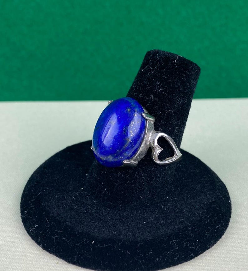 Op de afbeelding: Een zilveren ring met een grote ovale lapis lazuli-steen gezet in een hartvormig ontwerp.