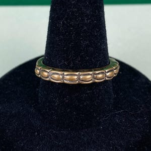 Peut inclure: Une bague dorée avec un motif texturé de forme ovale. La bague est sur un présentoir noir.
